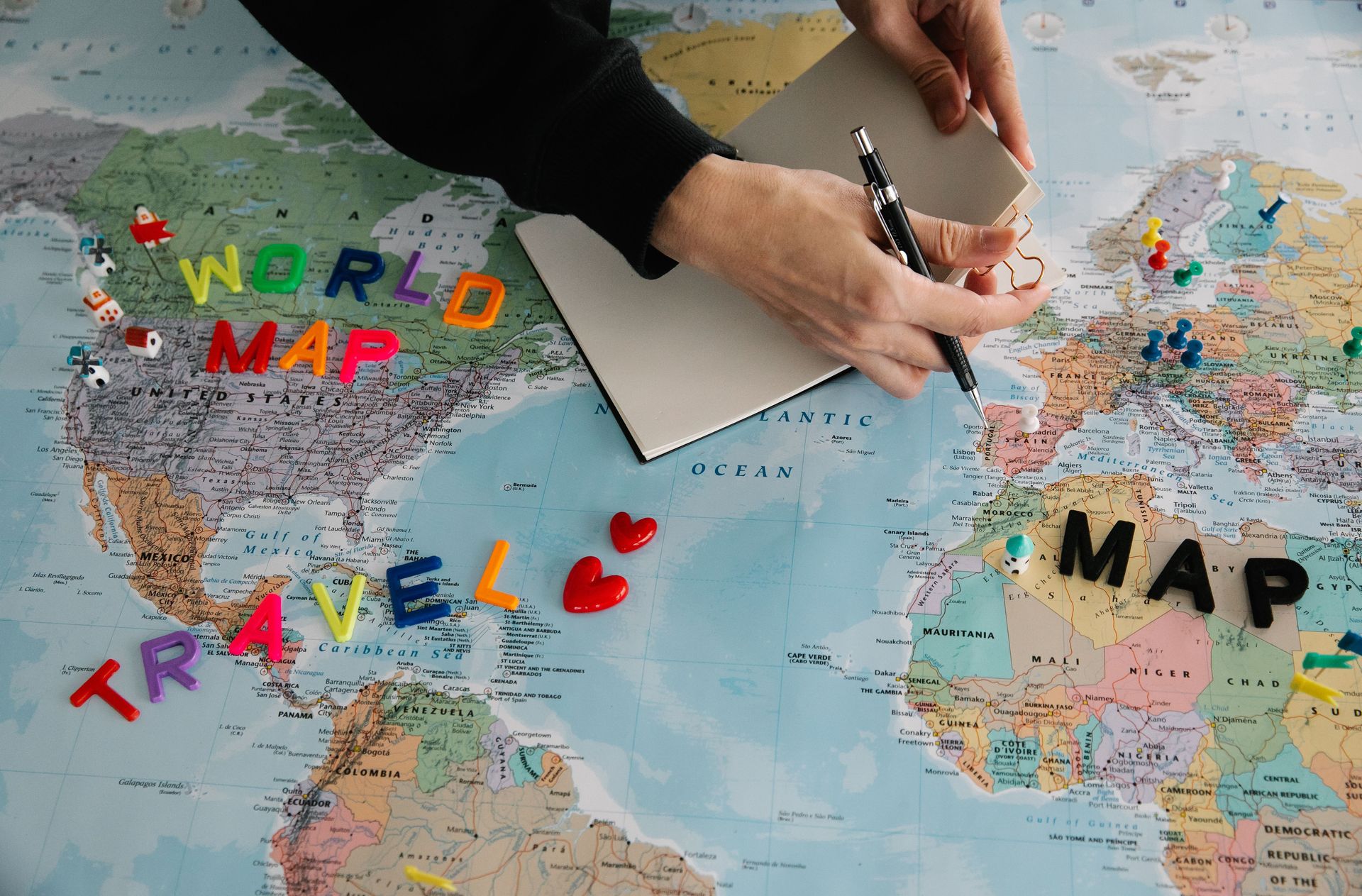 Hands holding pen and notebook over vibrant world map planning a journey.